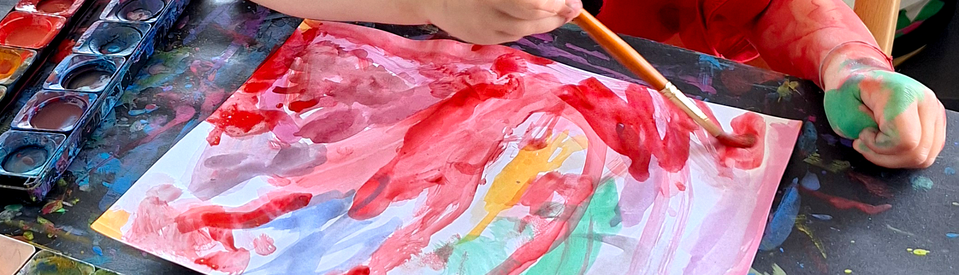 Kinderhände, die ein Bild mit Wasserfarben malen.